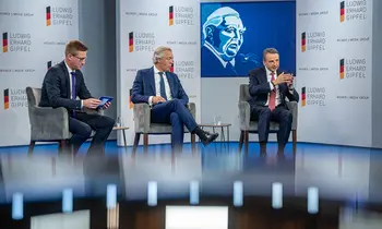 Drei Männer sitzen bei einer Podiumsdiskussion auf einer Bühne mit Ludwig-Erhard-Gipfel-Logos.