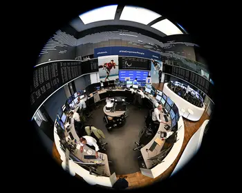 Mehrere Händler sitzen an Monitoren in einem kreisförmig wirkenden Handelssaal, aufgenommen mit einem Fisheye-Objektiv, im Hintergrund Kursanzeigen und Bildschirme.