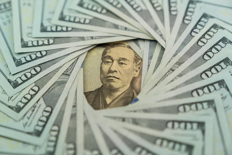 Eine japanische 10.000-Yen-Banknote liegt in der Mitte, kreisförmig umgeben von aufgefächerten 100-US-Dollar-Scheinen.