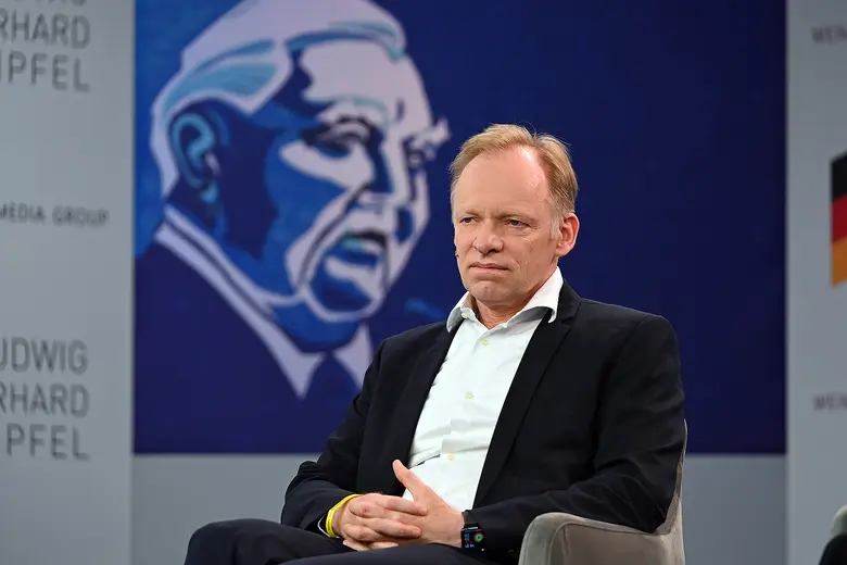 Clemens Fuest sitzt in Anzug und Hemd auf einem Podium.