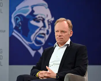 Clemens Fuest sitzt in Anzug und Hemd auf einem Podium.