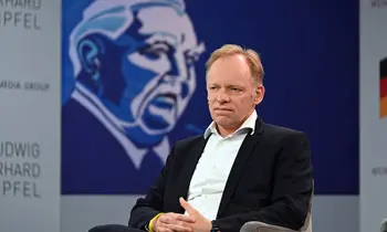 Clemens Fuest sitzt in Anzug und Hemd auf einem Podium.