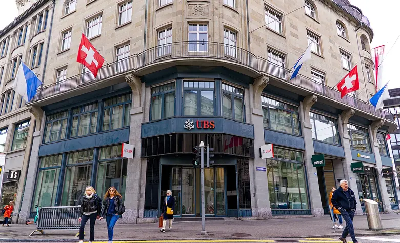Eingang einer UBS-Filiale an der Bahnhofstrasse in Zürich mit Passanten und Schweizer Fahnen.